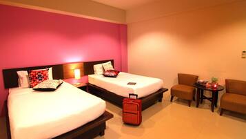 A hotel room with two beds, a small table with a lamp, and a chair.