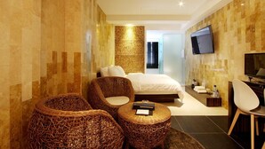 A modern hotel room with a large bed, two wicker chairs, a small round table, a TV, and a minibar. - Rich Diamond Hotel (Seoul)