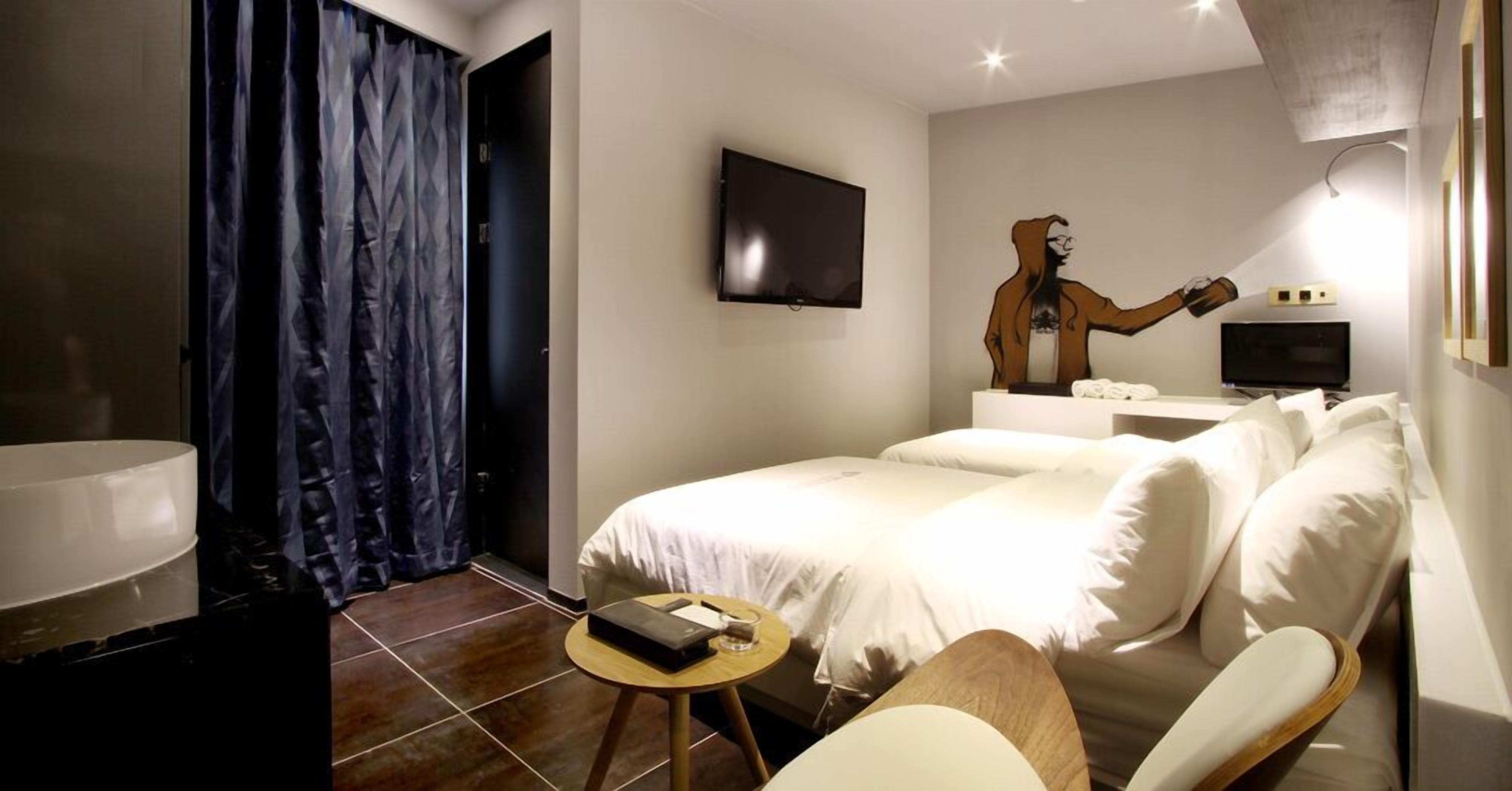 A hotel room with a bed, a desk, a chair, a TV, and a wall-mounted artwork.