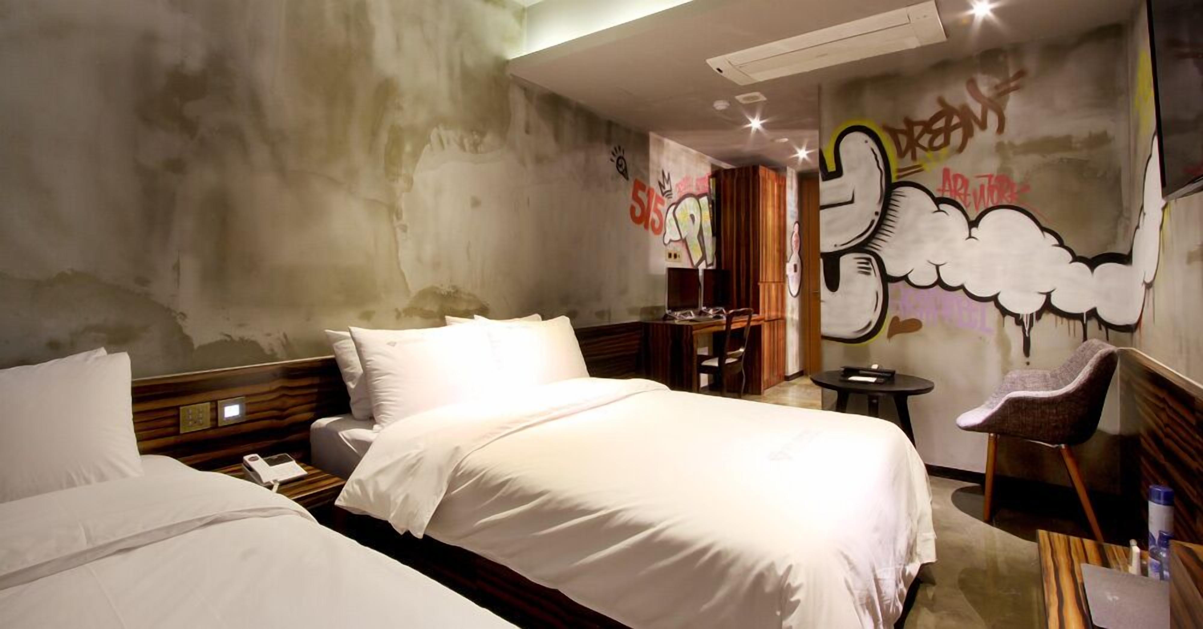 A hotel room with a bed, a desk, a chair, and a wall with graffiti art.