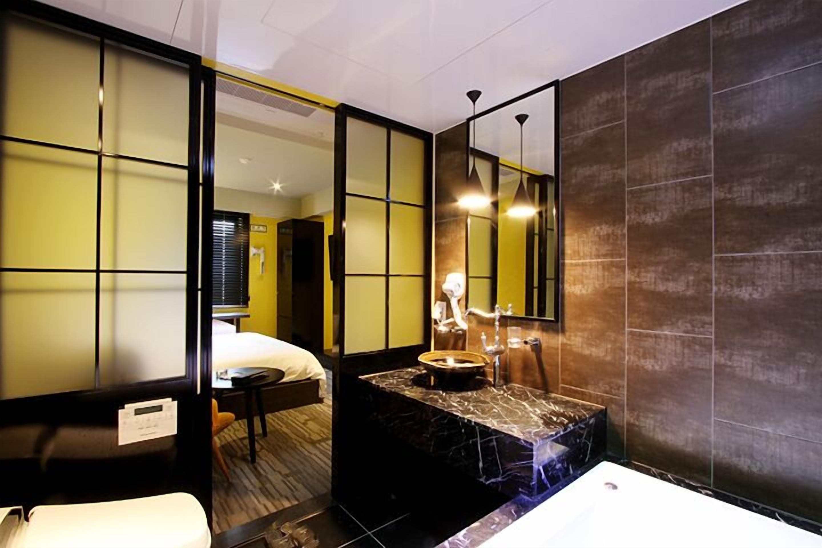 Een moderne hotelkamer met een groot bed, een apart zithoekje, een badkamer met een marmeren wastafel en een grote spiegel.