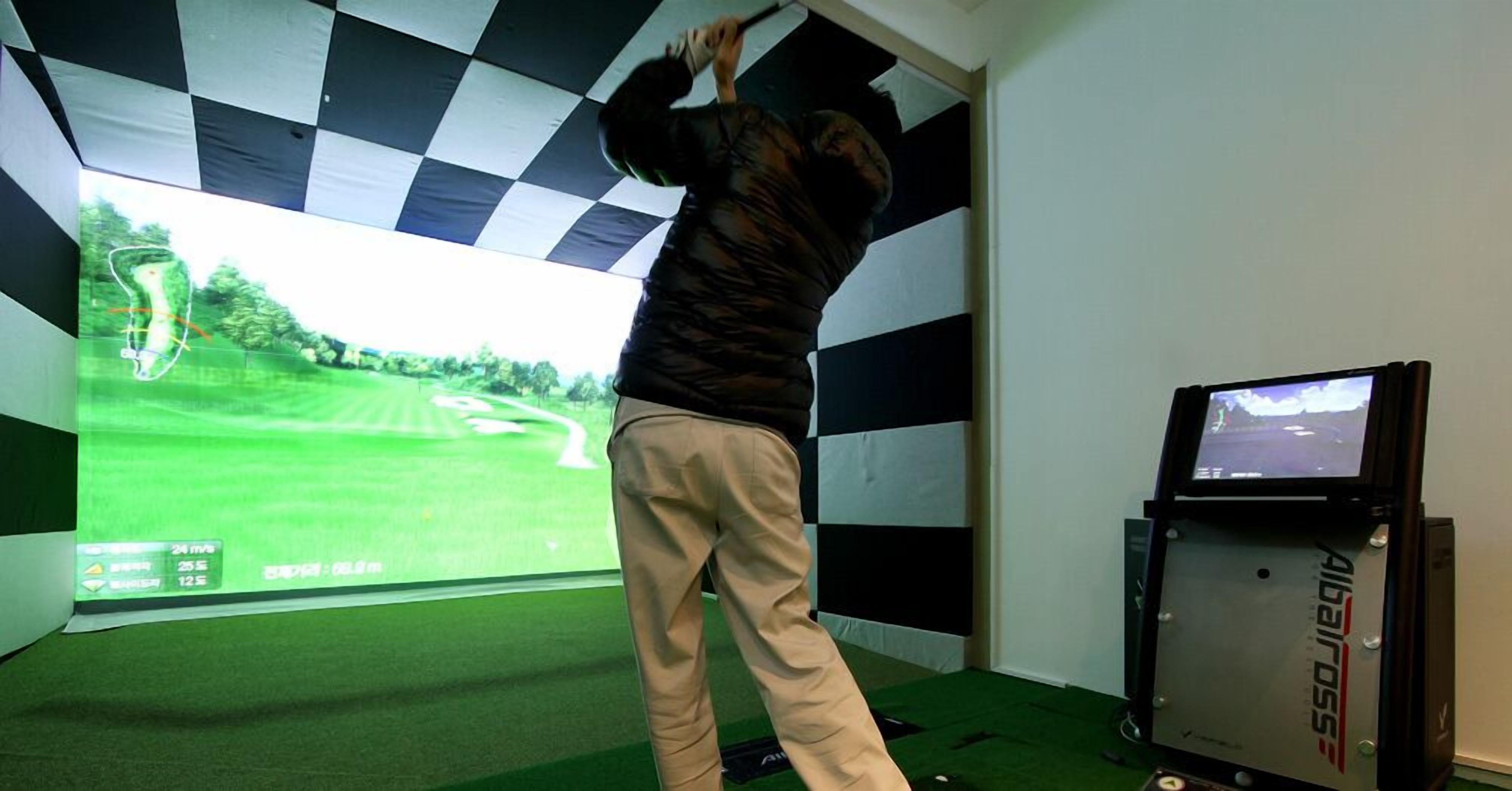 Eine Person spielt Golf in einem Innenbereich, während ein großer Bildschirm einen Golfplatz zeigt.