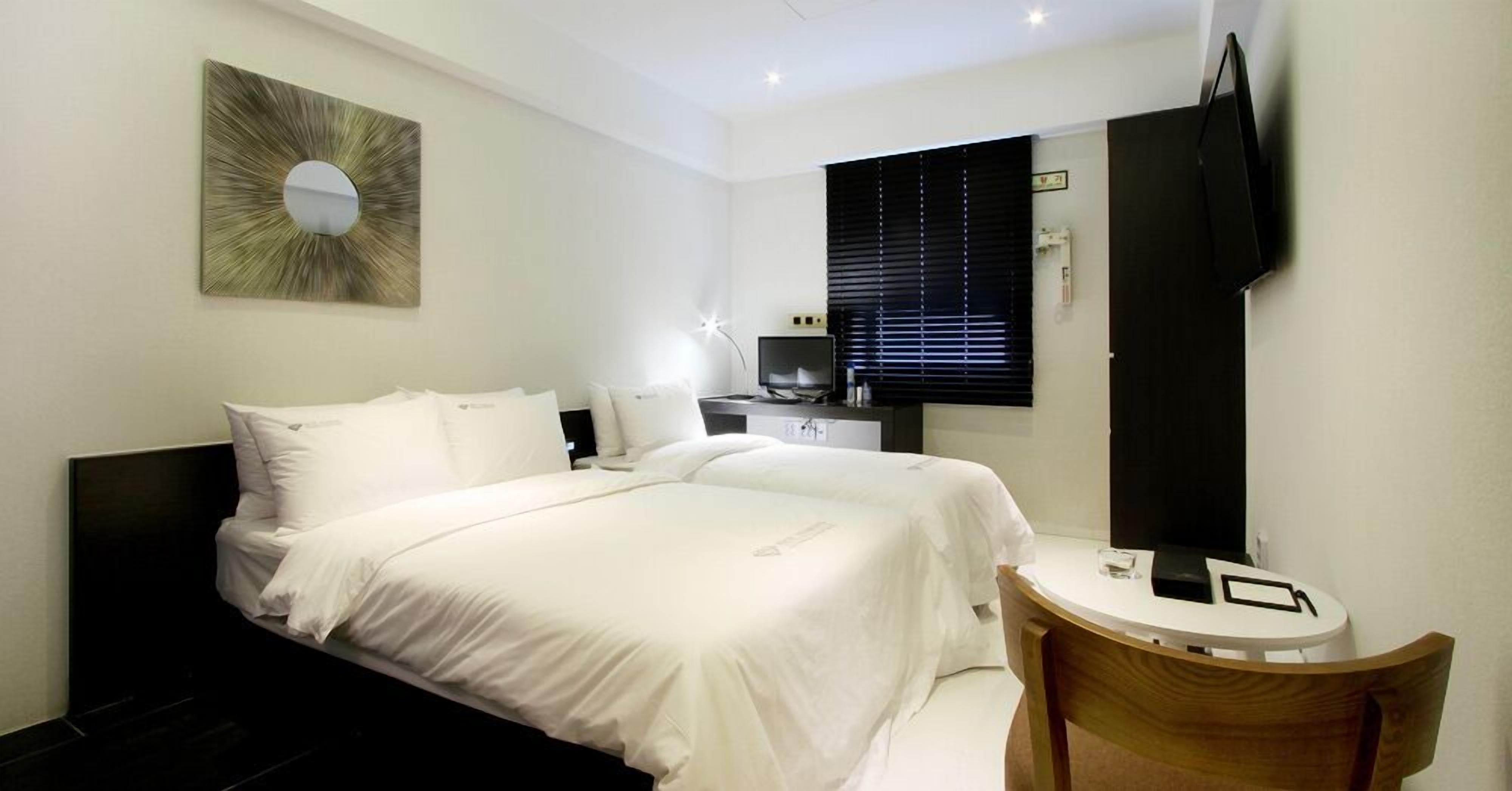 A hotel room with a bed, a desk, a chair, a TV, and a window with blinds.