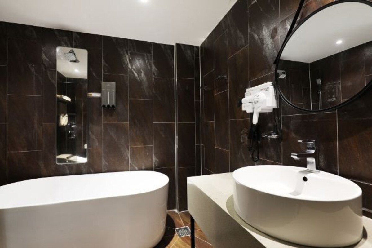 A modern bathroom with dark marble walls, a large freestanding bathtub, and a round sink with a mirror above it.