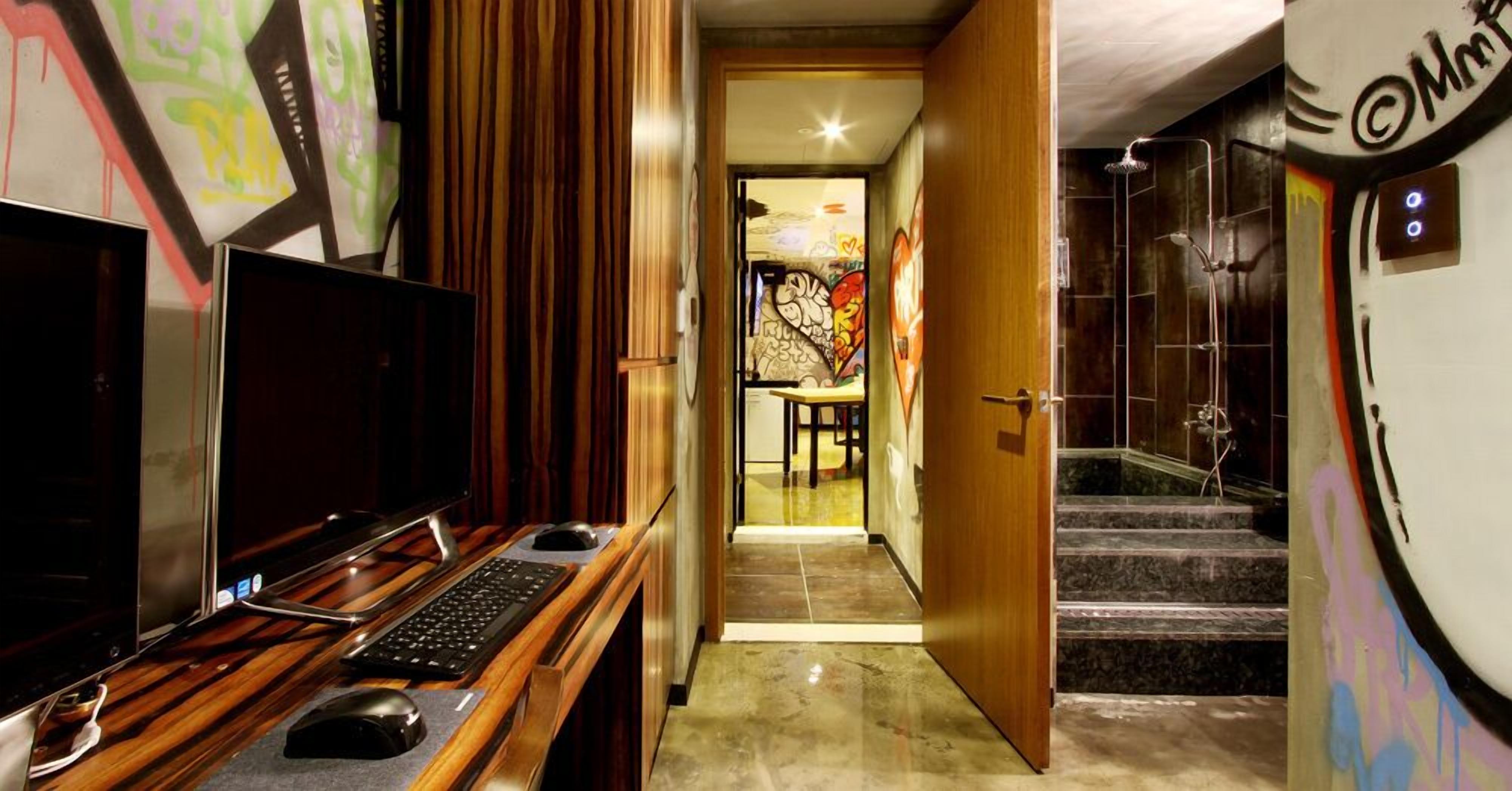 A hotel room with a wooden desk, a television, and a shower area with graffiti.