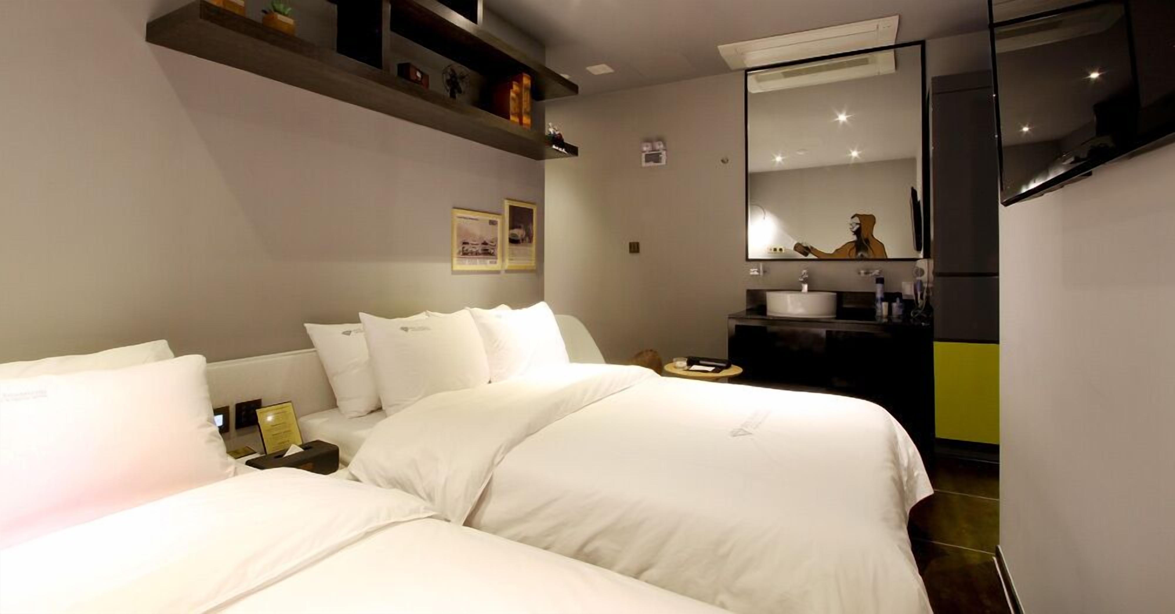 Una habitación de hotel con dos camas, un baño con lavamanos y un espejo grande.