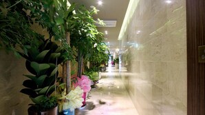 A corridor with potted plants on one side and a marble wall on the other. - Rich Diamond Hotel (Seoul)
