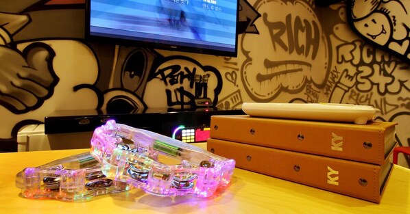 Configuración de videojuegos con un control translúcido iluminado, un monitor mostrando un juego y una pared con grafiti.