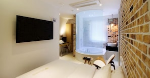 Quarto de hotel moderno com televisão de tela plana, uma banheira grande, parede de tijolos e uma pequena mesa de trabalho com cadeira.