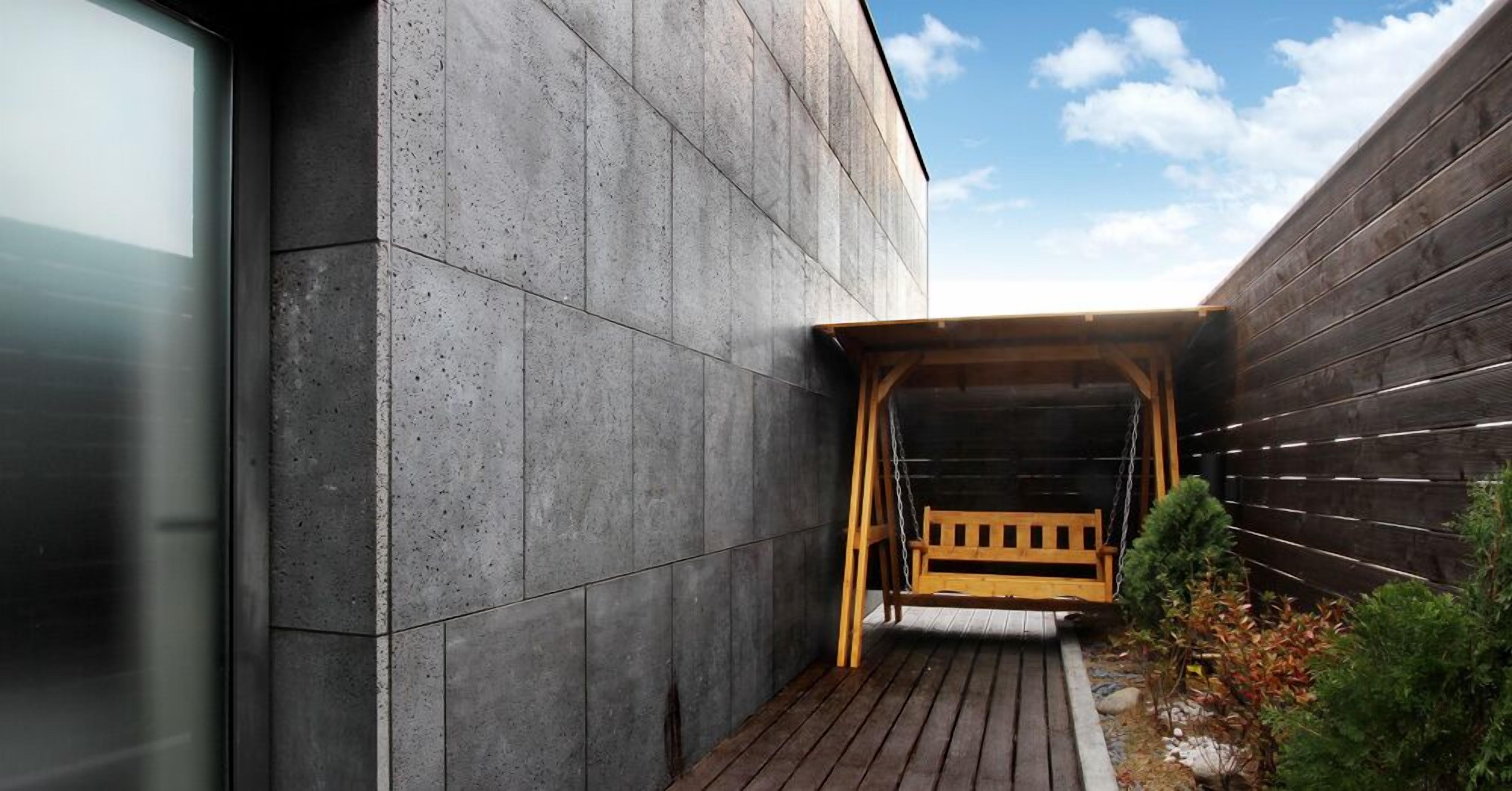 A modern building with a concrete exterior and a wooden swing bench in a covered outdoor area.