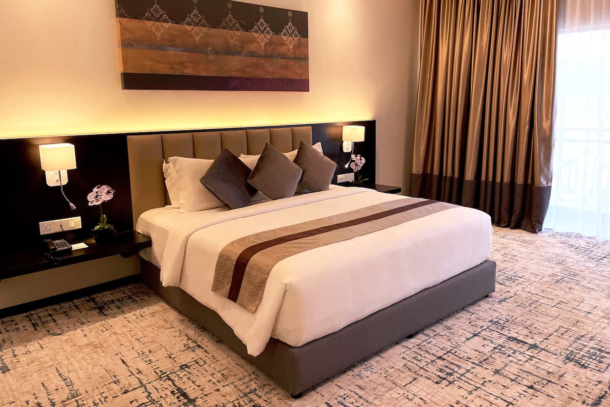 Een hotelkamer met een groot bed, een hoofdeinde met een lamp, een nachtkastje met een telefoon en lamp, en een raam met gordijnen.