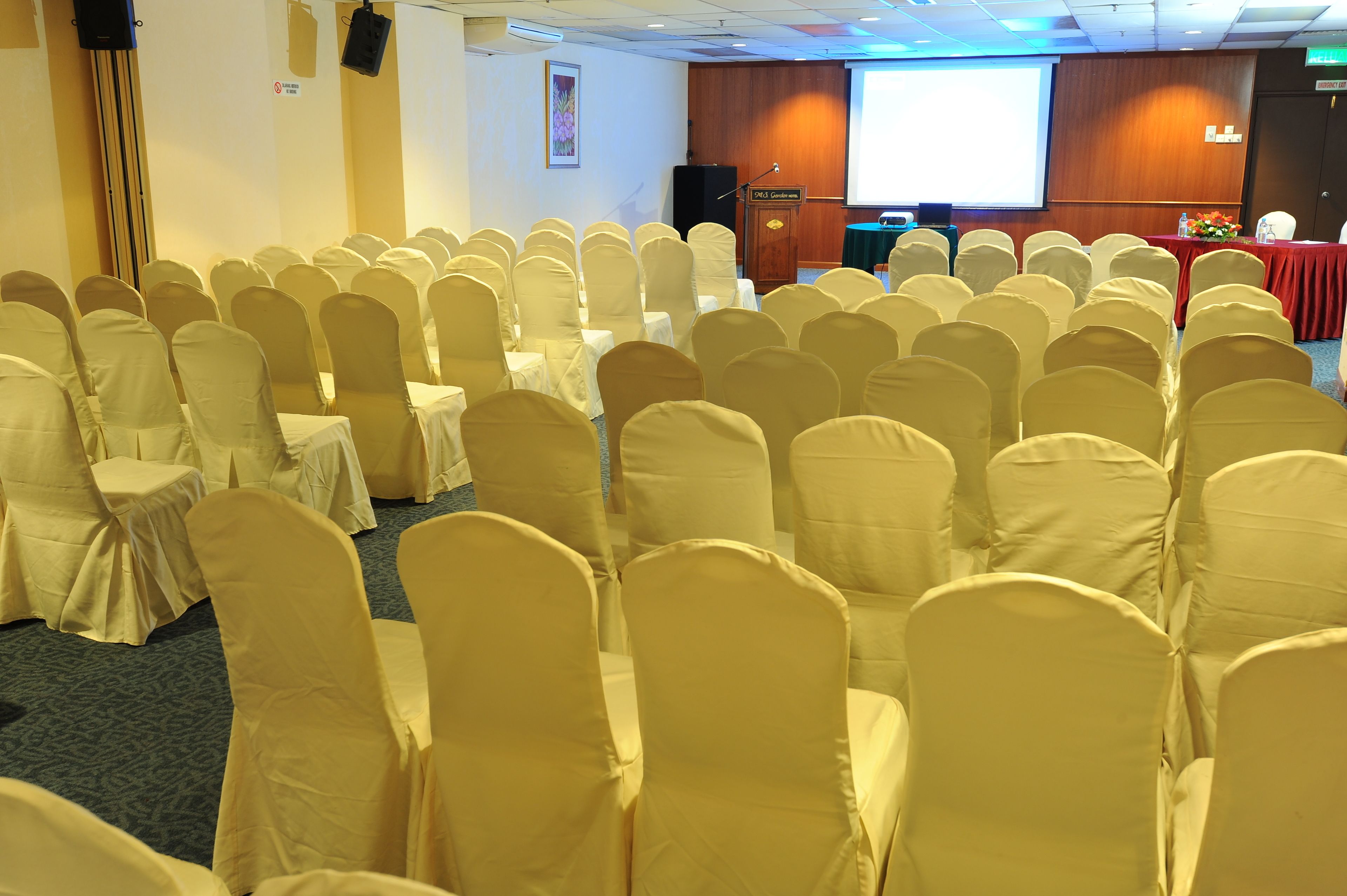 A conference room with rows of chairs covered in white fabric, a podium, and a screen in the background.