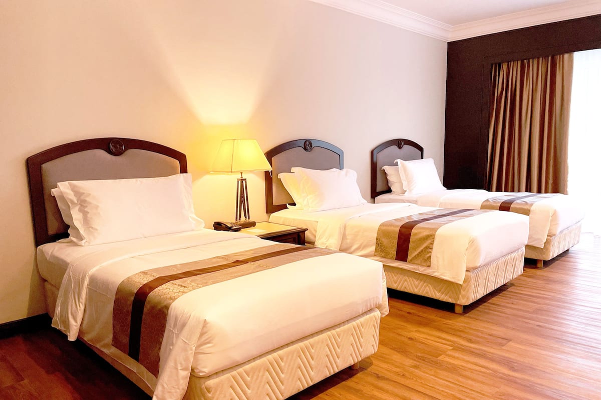 Een hotelkamer met drie bedden, een nachtkastje met een lamp en houten vloeren.