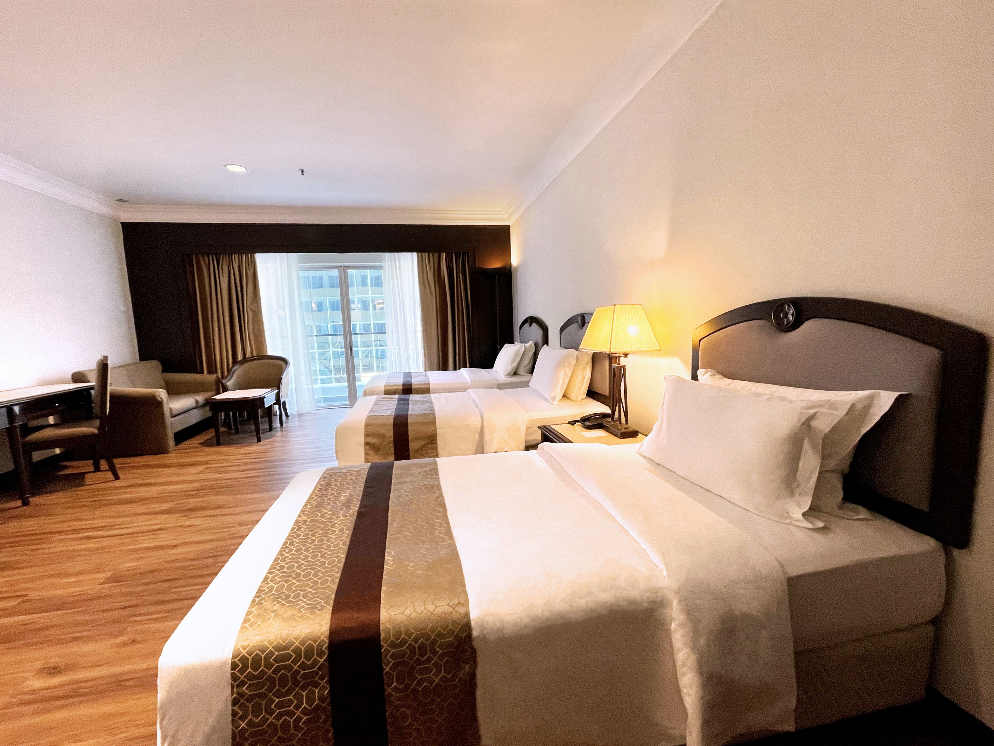 A hotel room with two beds, a desk, a chair, and a view of the city through a large window.