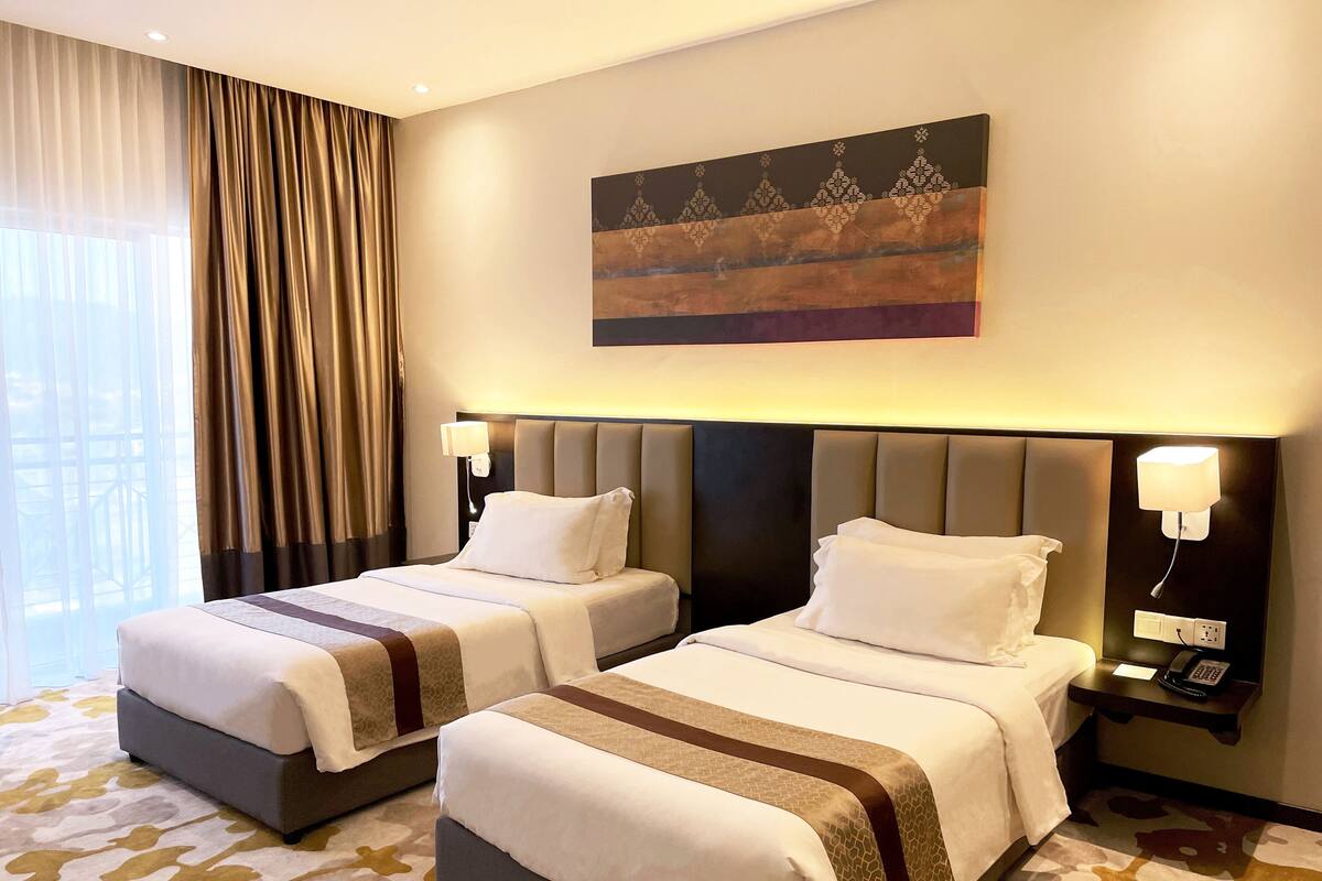 Een hotelkamer met twee bedden, een schilderij aan de muur en een kamerbreed tapijt met een patroon.