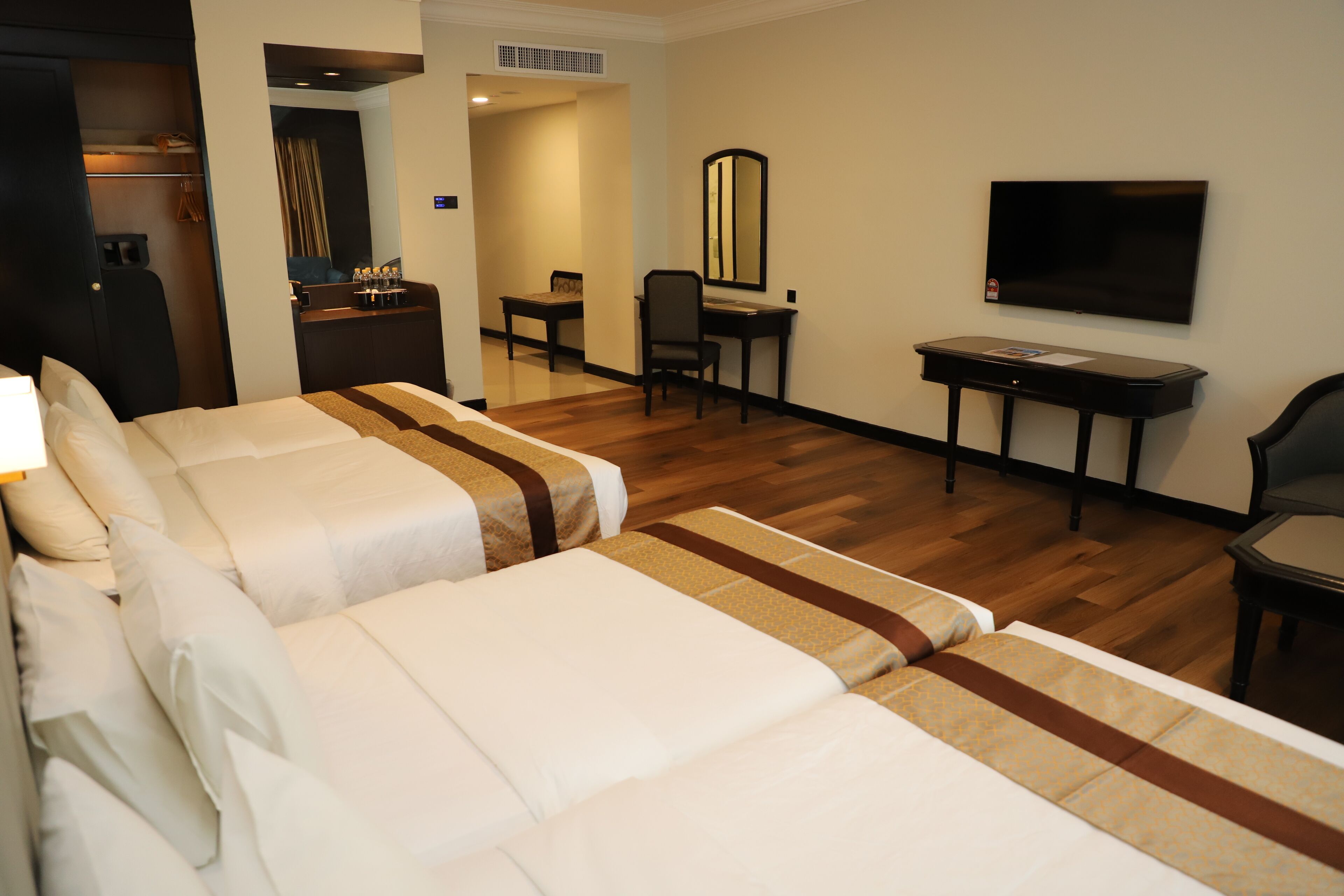 Une chambre d’hôtel avec deux lits, un bureau, une chaise, une télévision et une salle de bain visible à travers une porte ouverte.