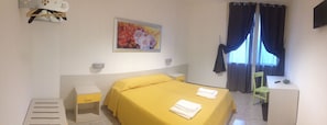 Una habitación de hotel con cama, mesita de noche, sillón, escritorio y un cuadro en la pared.