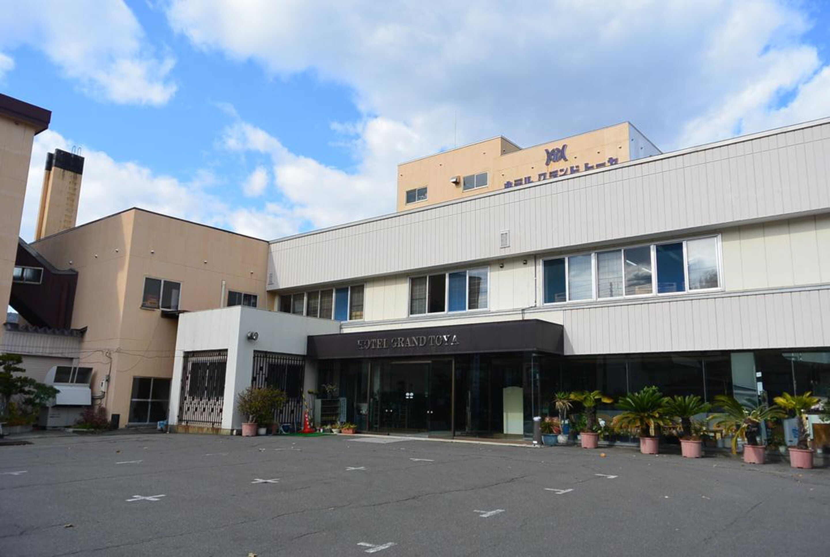 A hotel with a modern facade, large windows, and a parking lot with potted plants.
