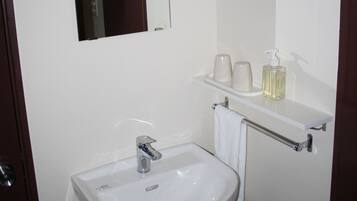 Un baño con un lavamanos blanco, un espejo y un estante con artículos de aseo.