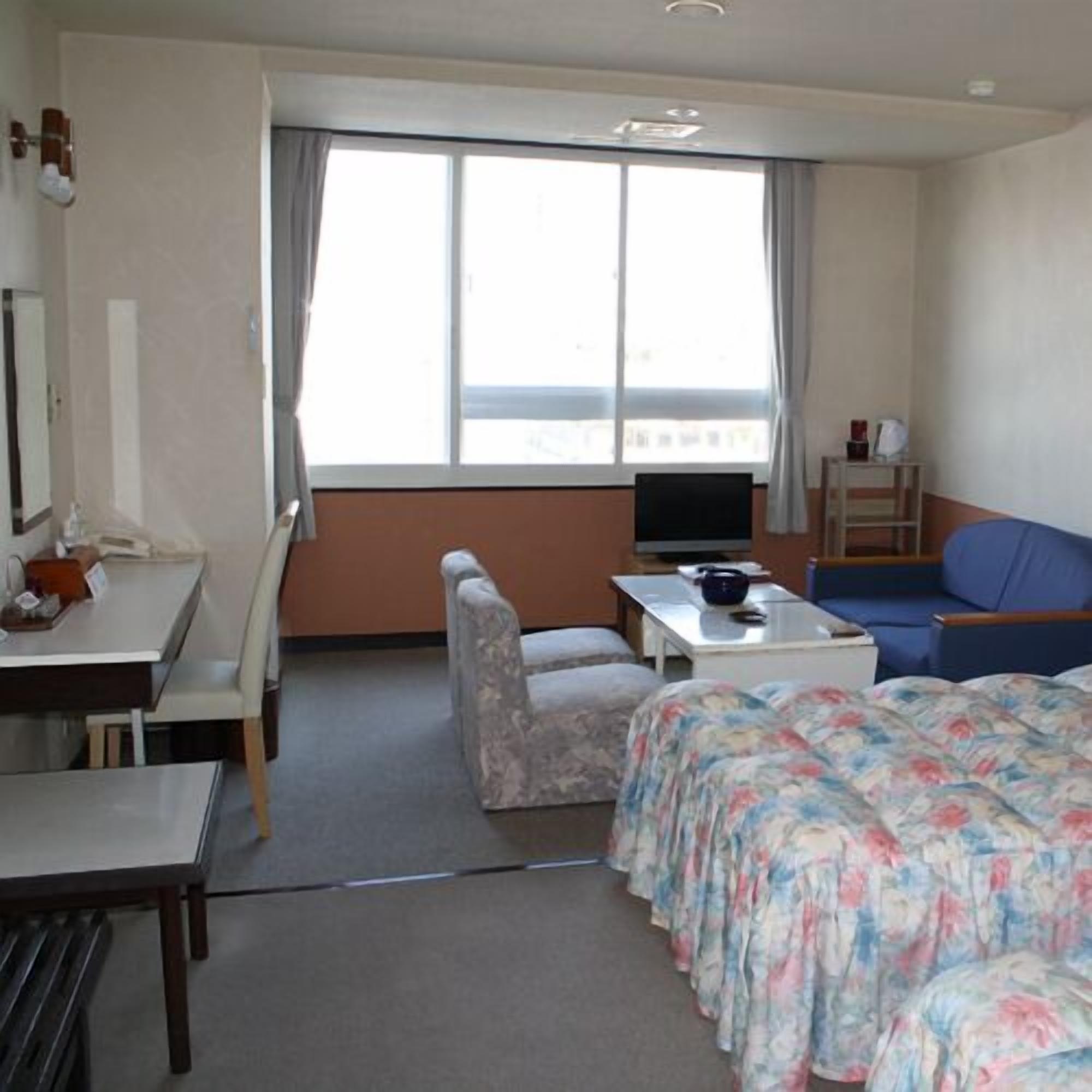 A hotel room with a bed, a desk, a chair, a television, and a sofa.