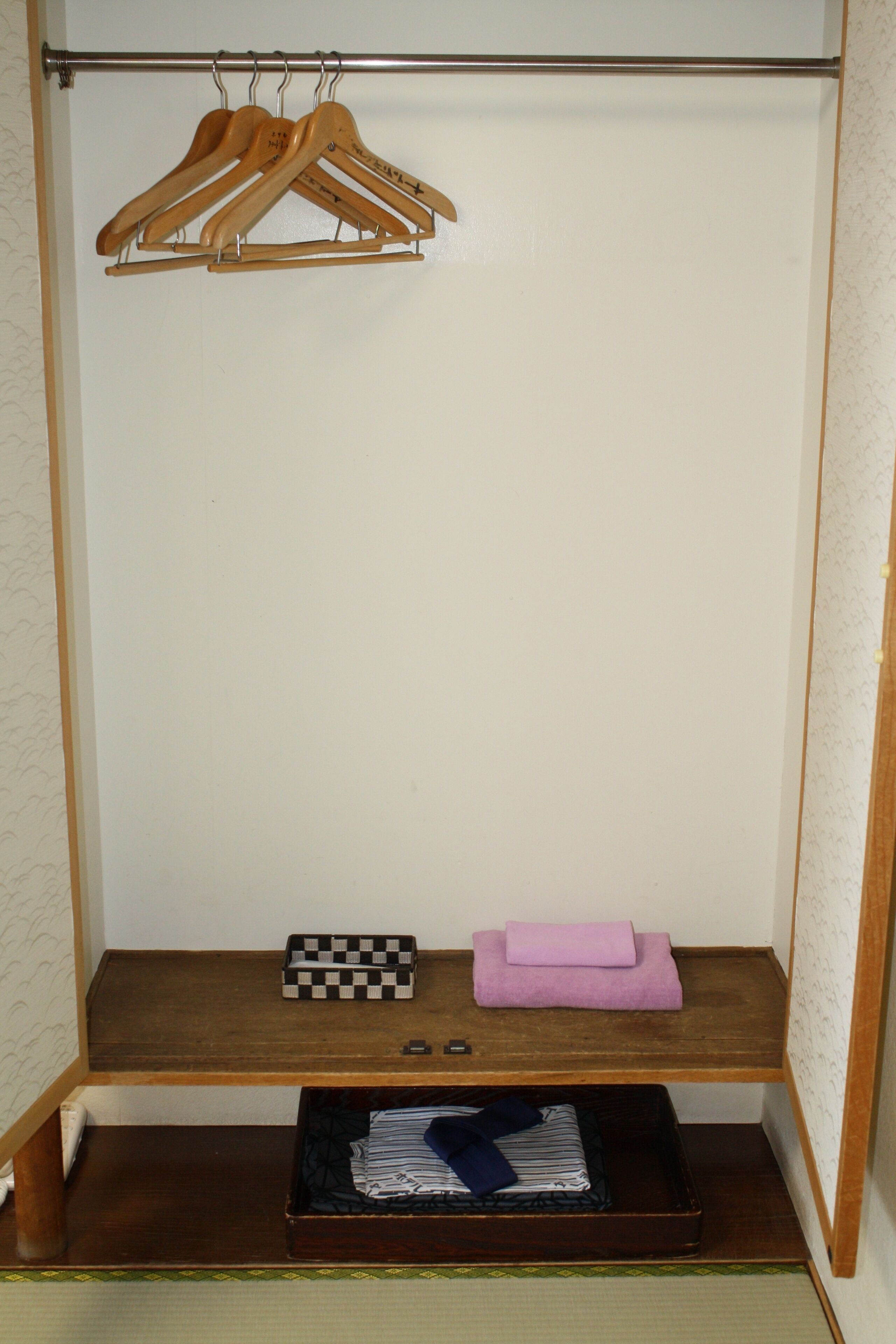 A closet with wooden hangers, a checkered box, a folded towel, and a suitcase on a shelf.