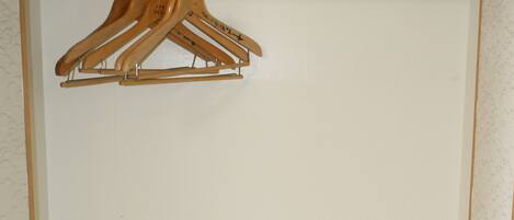 A closet with wooden hangers, a checkered box, a folded towel, and a suitcase on a shelf.