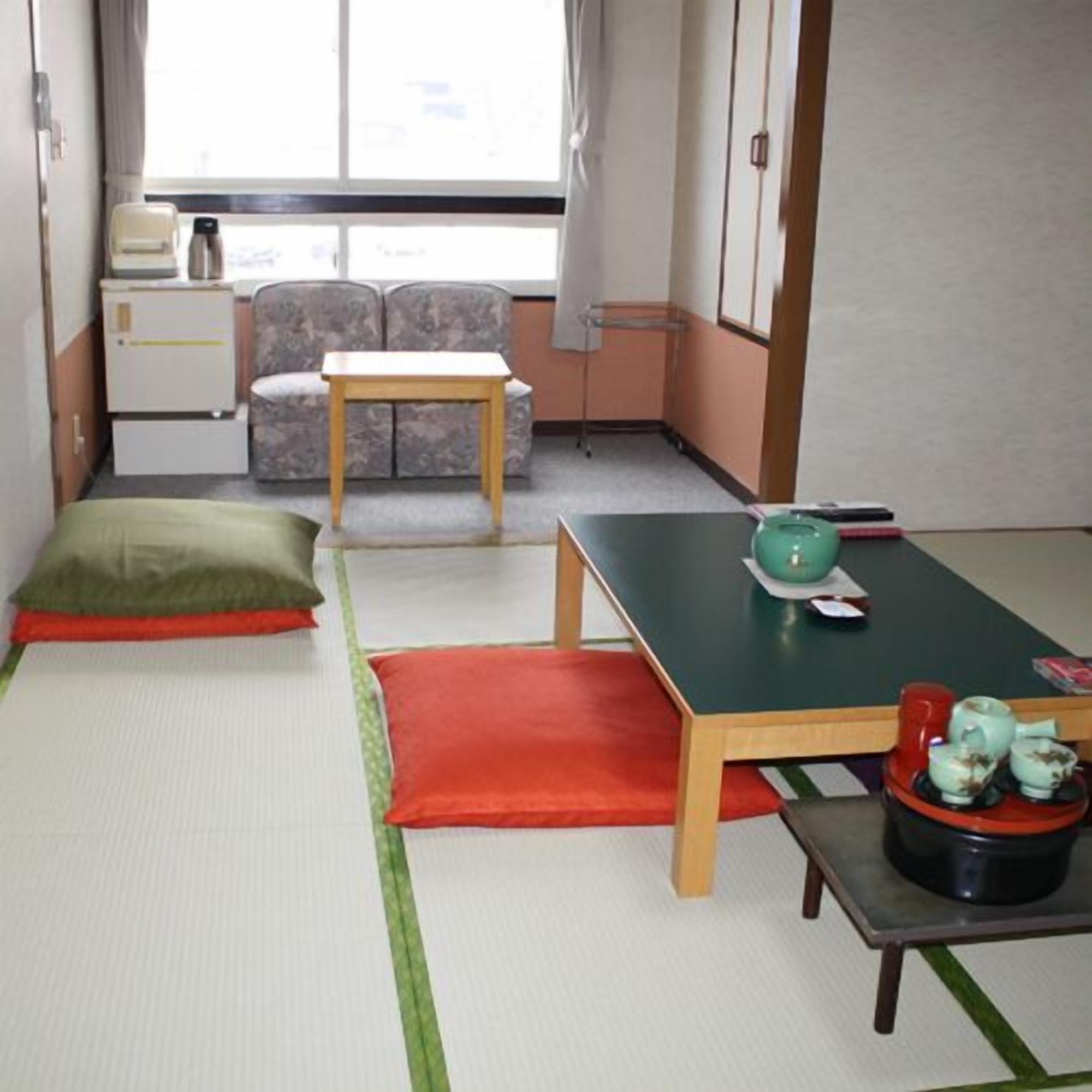 A room with tatami flooring, a futon bed, a small table with a green bowl, and a futon sofa.