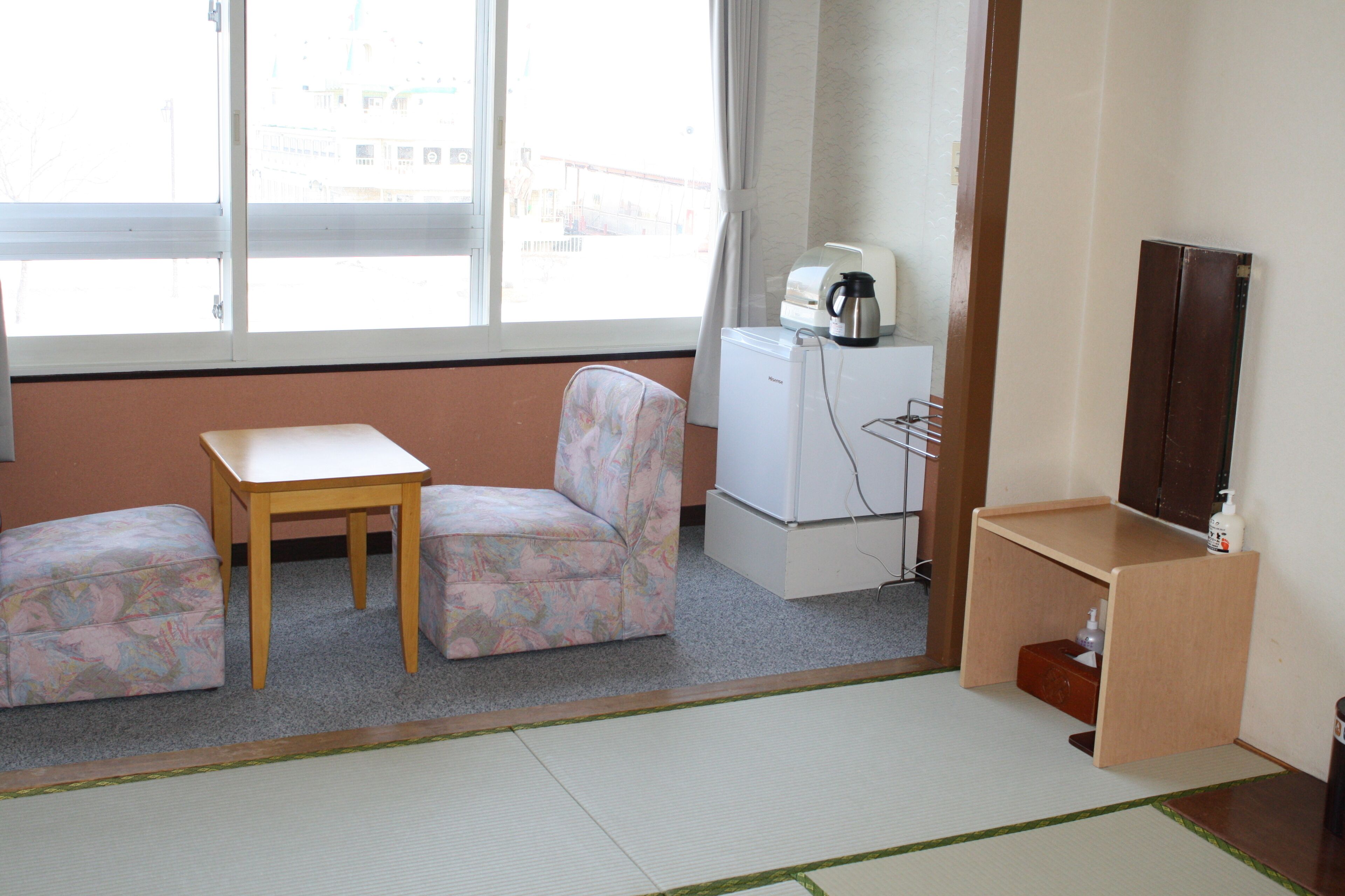 A small hotel room with a sofa, a table, a coffee maker, and a TV.
