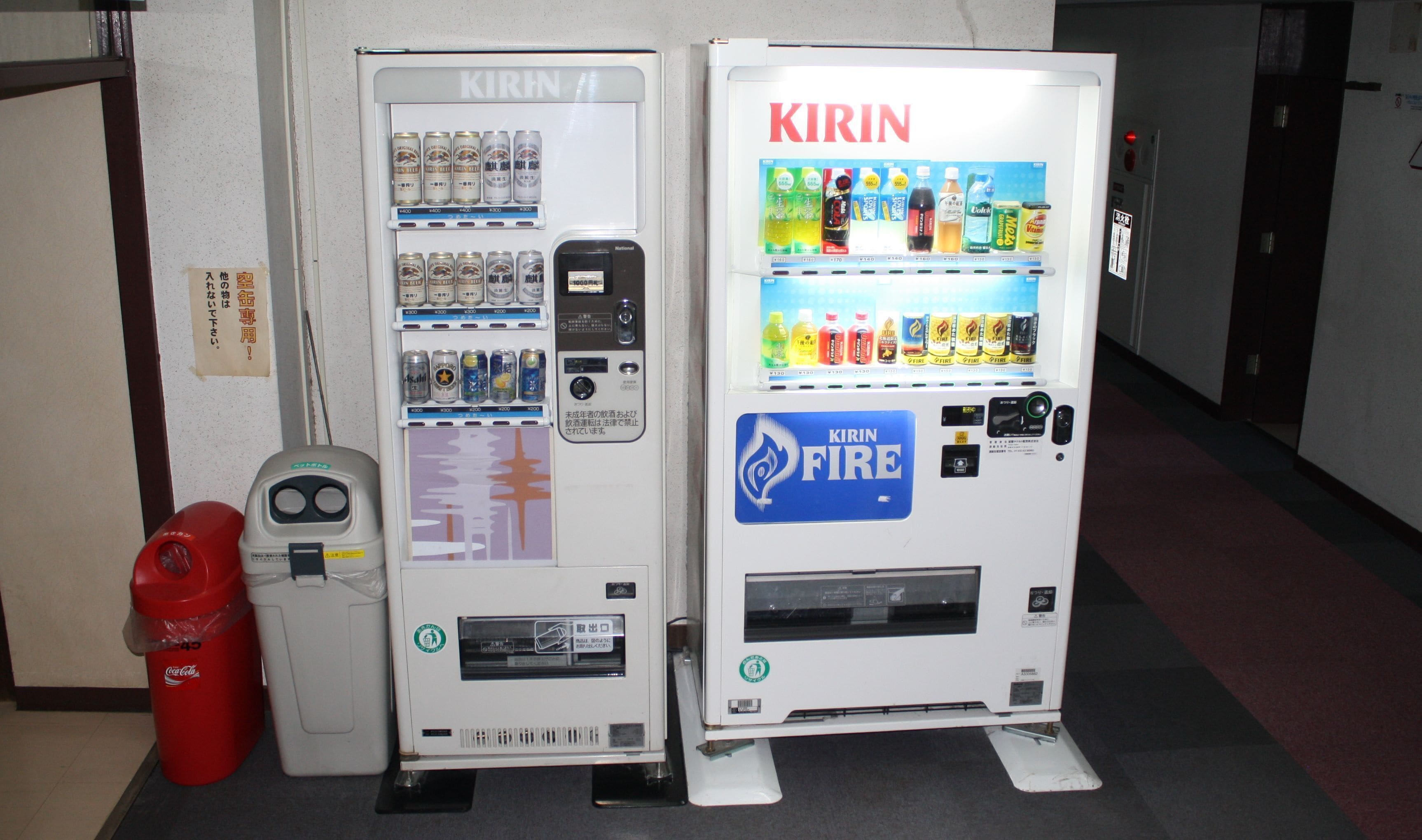 Two Kirin vending machines in a hallway, one with cans and the other with beverages.