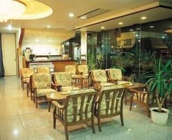 A hotel lobby with wooden chairs and tables, a reception desk, and a large window with a view of the outside.