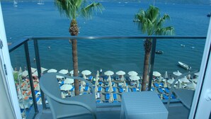 Un balcon doté de chaises longues et de parasols, donnant sur une étendue d’eau où se trouvent des bateaux.