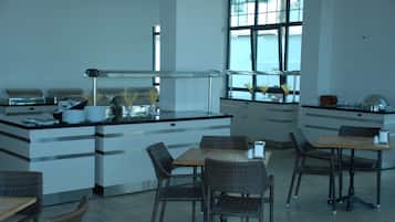 A modern kitchen area with a buffet setup, including a counter with food containers and a sink. There are wicker chairs and a table with a vase of flowers.