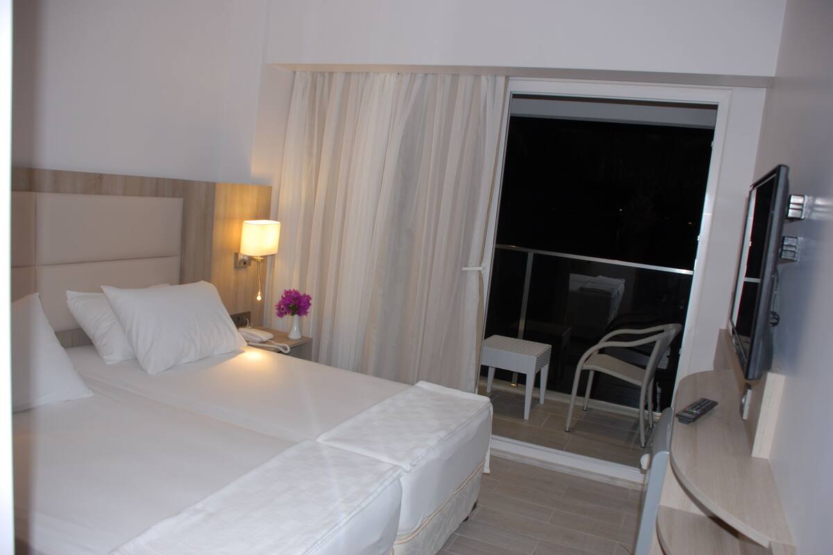 Ein Hotelzimmer mit einem großen Bett, einem Nachttisch mit Lampe, einem kleinen Tisch mit Stuhl und einem Fernseher.