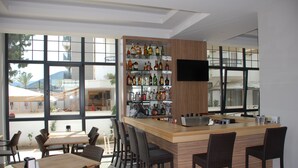 Un espace bar moderne avec un comptoir en bois, des tabourets de bar et une variété de bouteilles d’alcool. De grandes fenêtres offrent une vue sur l’extérieur.