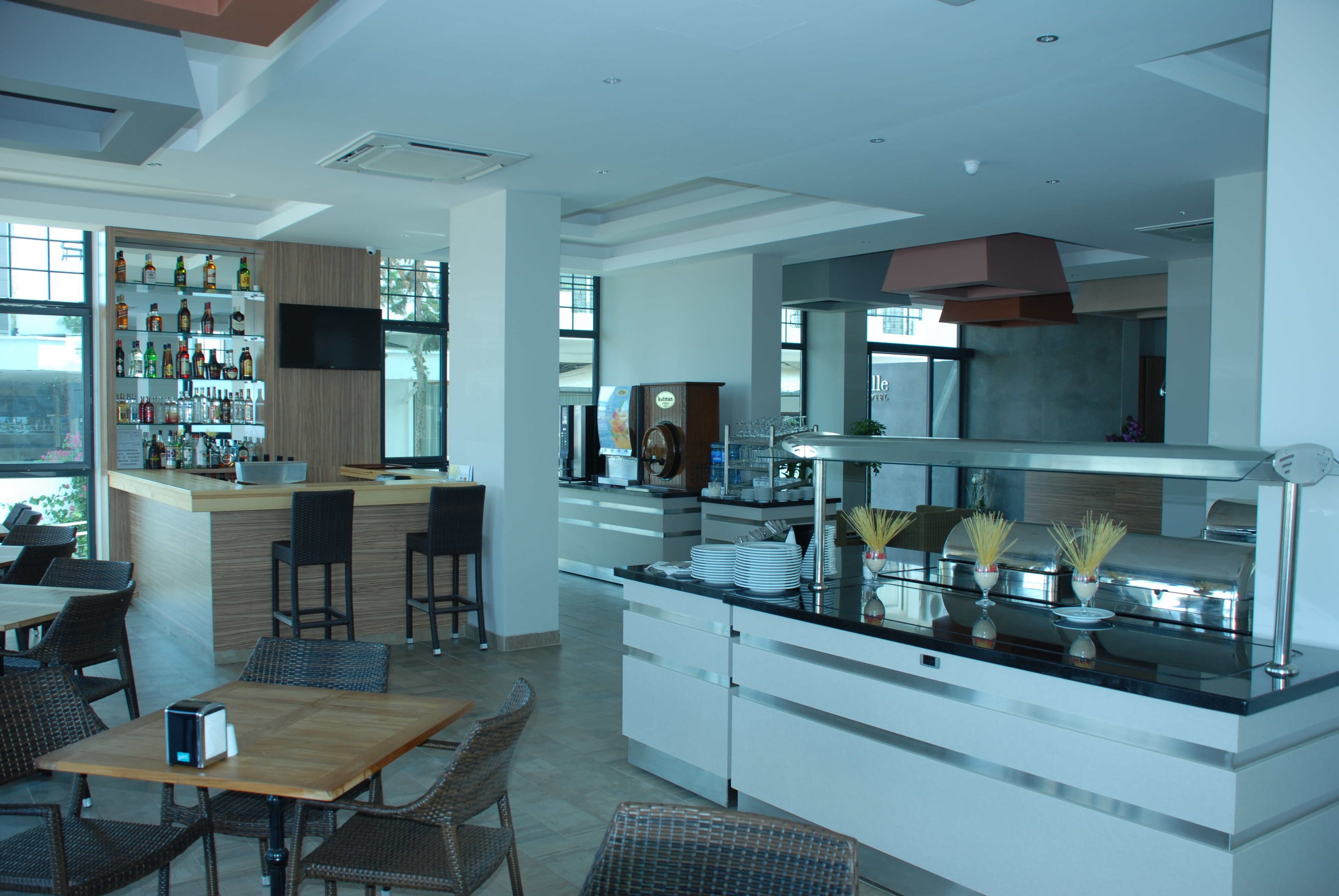 A modern restaurant with a bar area, dining tables, and chairs. There are shelves with bottles and a large screen mounted on the wall.