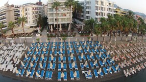 Un hôtel situé en bord de mer, avec plusieurs étages, des espaces de détente en plein air et des palmiers.