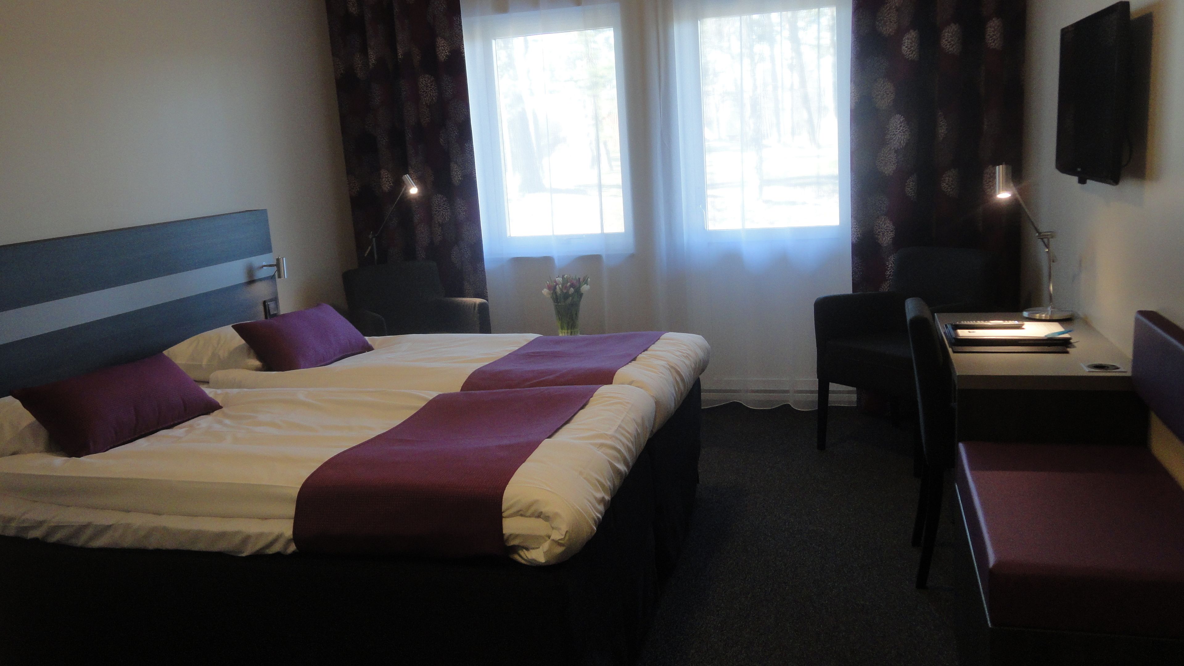 A hotel room with a large bed, a desk, a chair, and a TV mounted on the wall.