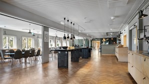 A spacious dining area with a long table, chairs, pendant lighting, and a kitchen area with cabinets and a countertop. - Tyleback Hotell & Konferens, BW Signature Collection (Halmstad)