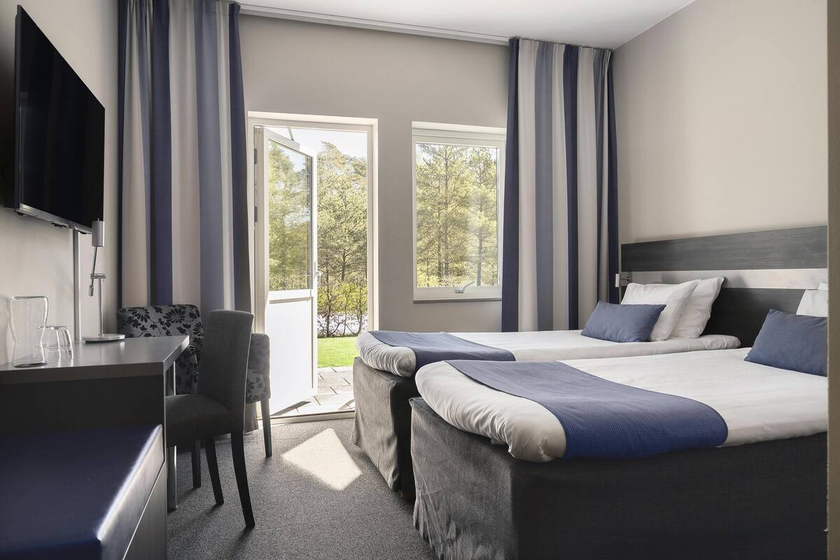 Een hotelkamer met twee bedden, een bureau, een stoel, een televisie en grote ramen.