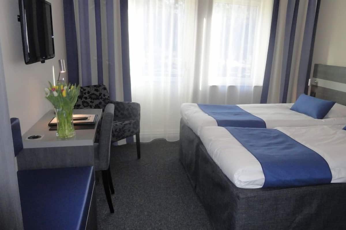 Een hotelkamer met twee bedden, een bureau, een stoel, een televisie en een raam met gordijnen.
