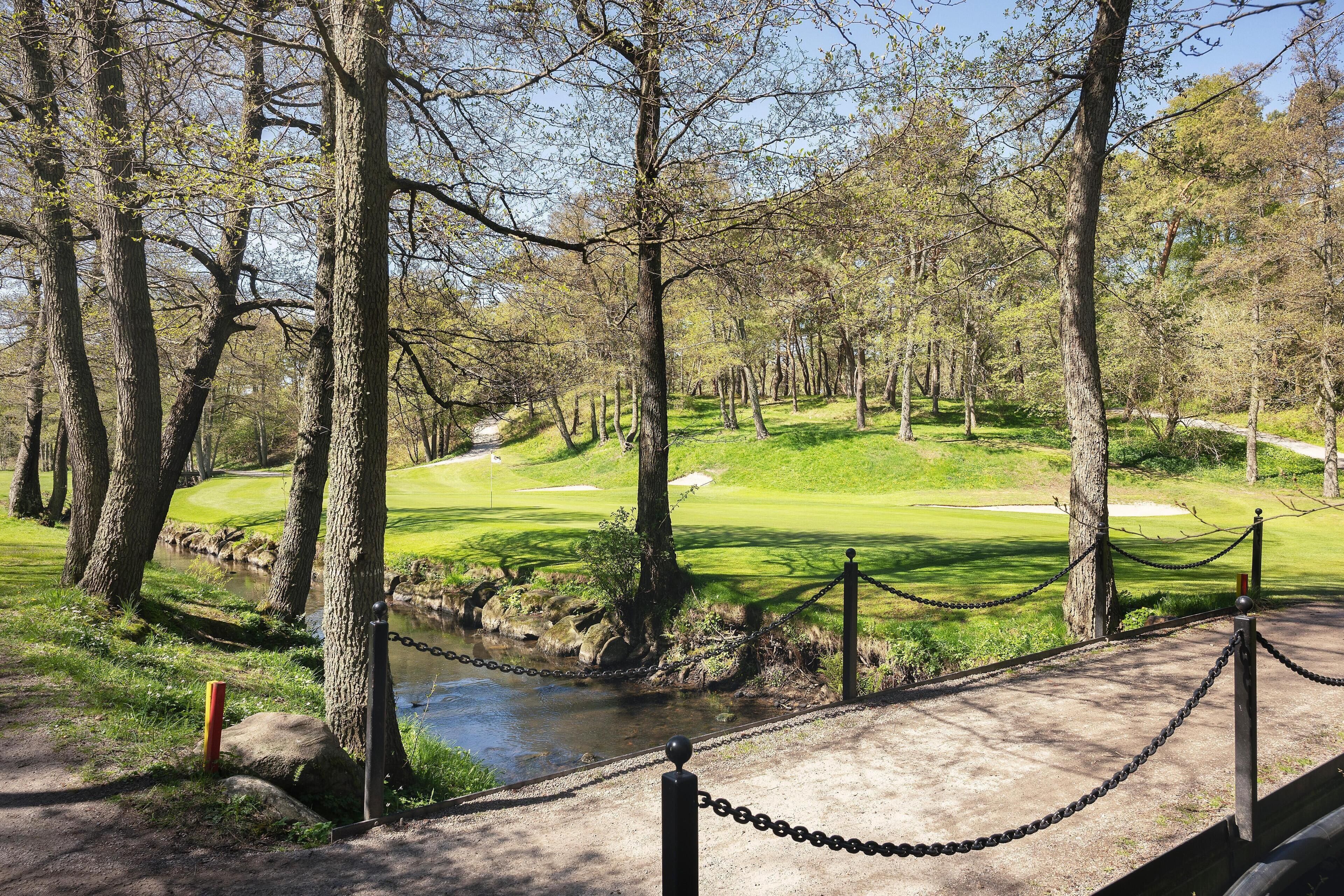 A golf course with a pond, surrounded by trees and a chain-link fence.