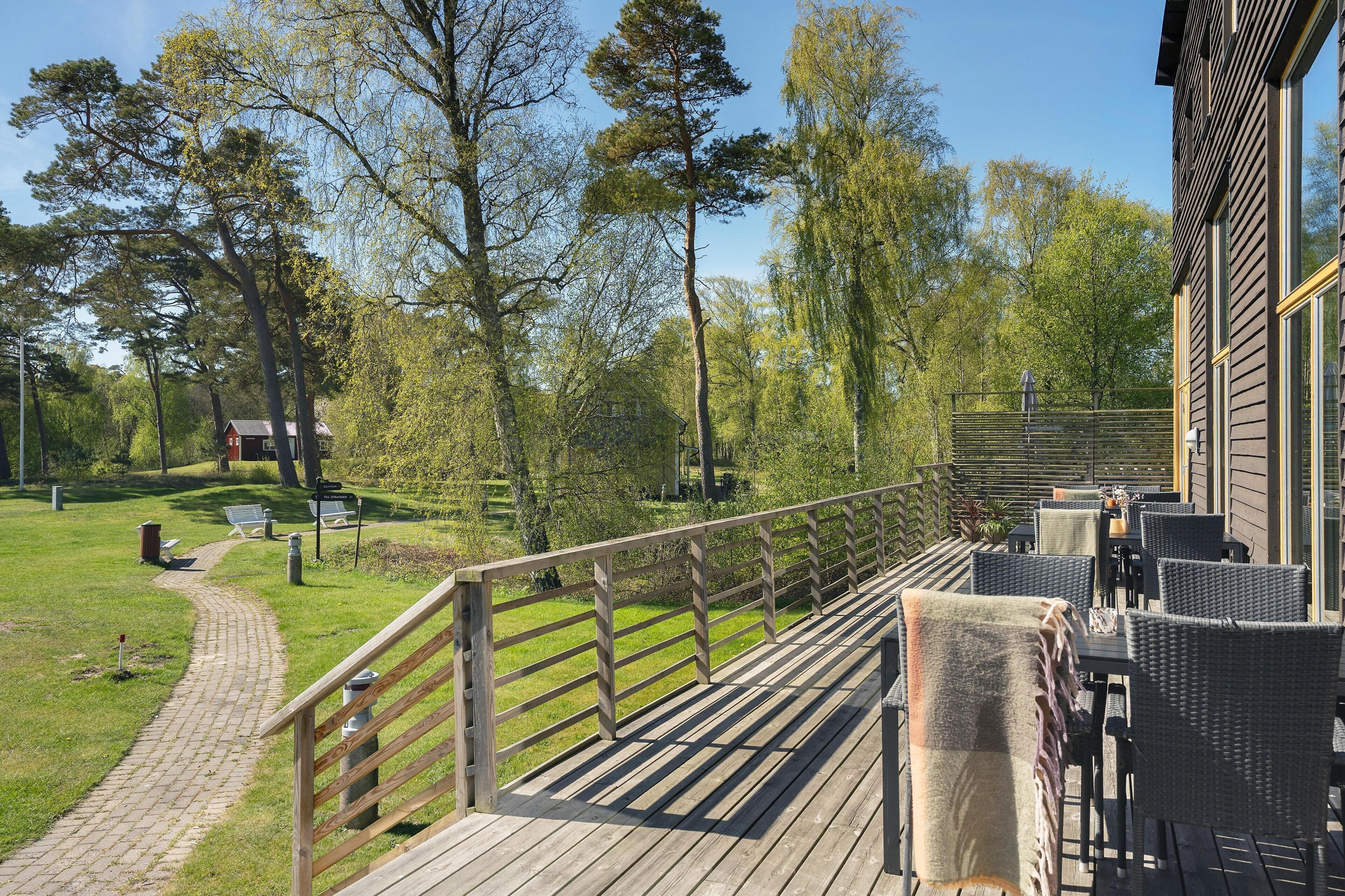 A wooden deck with outdoor seating, a pathway, and a view of trees and a building.