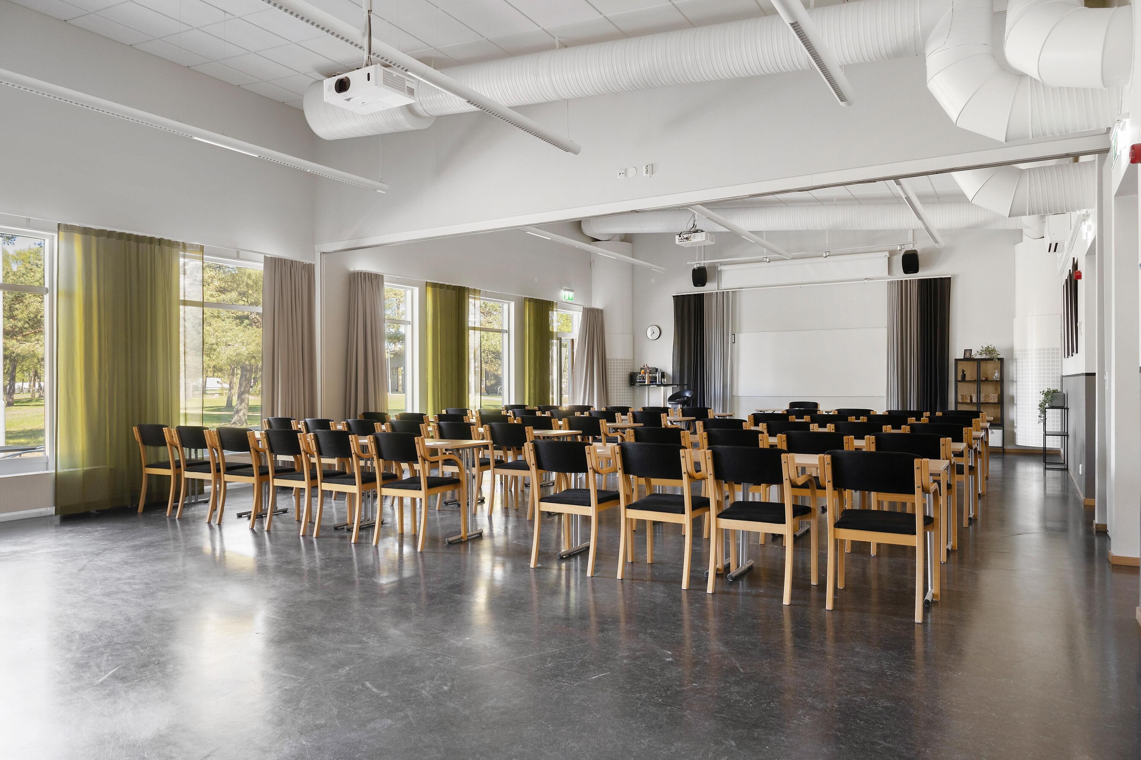 A conference room with rows of chairs, a projector, and large windows with curtains.