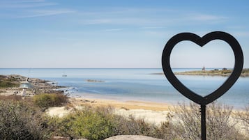 Una estructura metàl·lica amb forma de cor en primer terme, amb una platja i mar tranquil·la al fons.