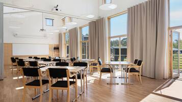 A conference room with tables and chairs, large windows, and a projector screen.