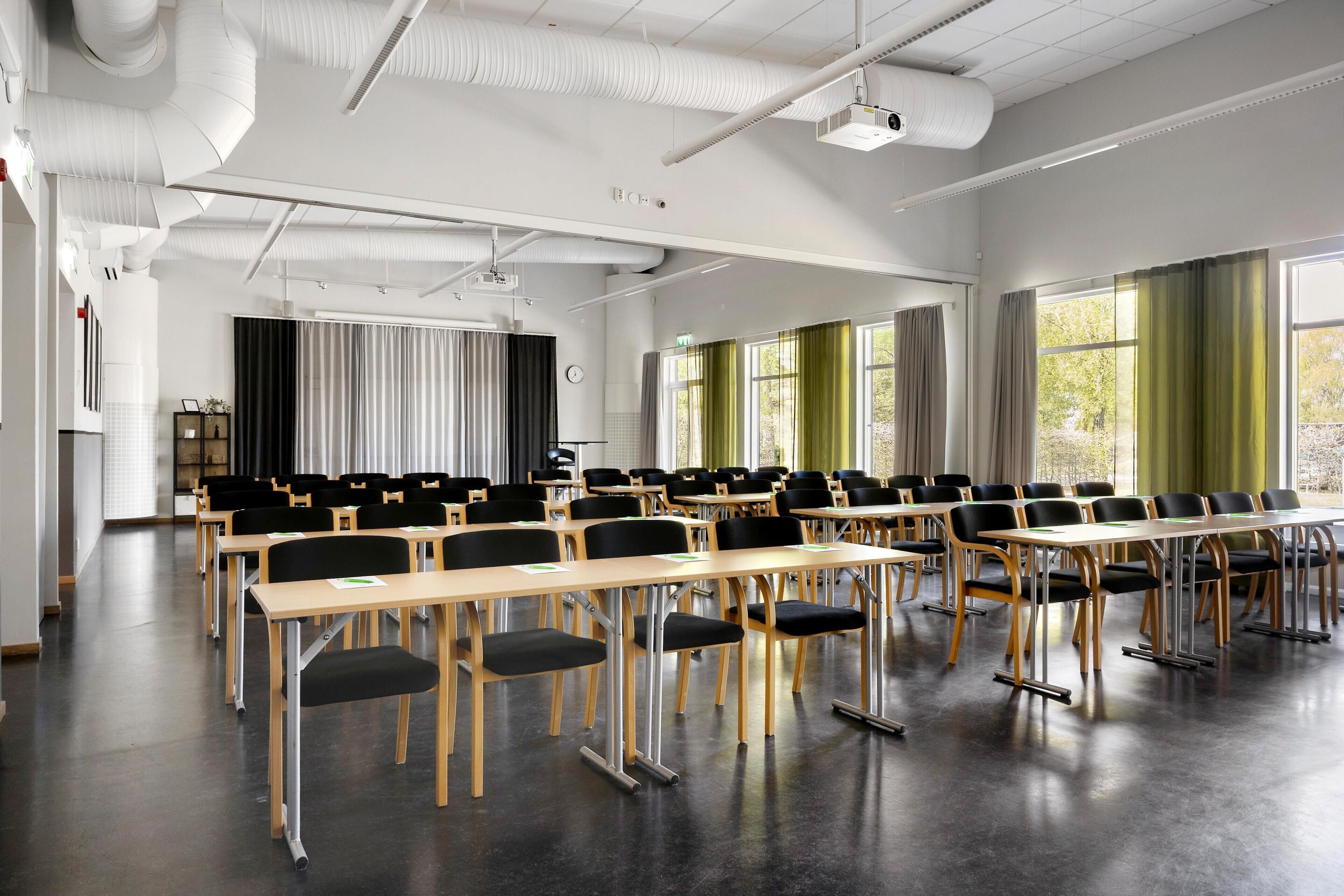 A conference room with rows of tables and chairs, large windows, and a projector.