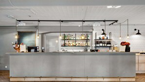 A modern bar area with a central counter, hanging pendant lights, and shelves stocked with bottles. - Tyleback Hotell & Konferens, BW Signature Collection (Halmstad)