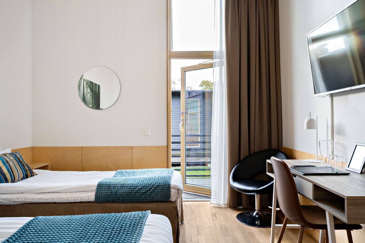 Een hotelkamer met twee bedden, een bureau, een stoel, een televisie en een groot raam met gordijnen.