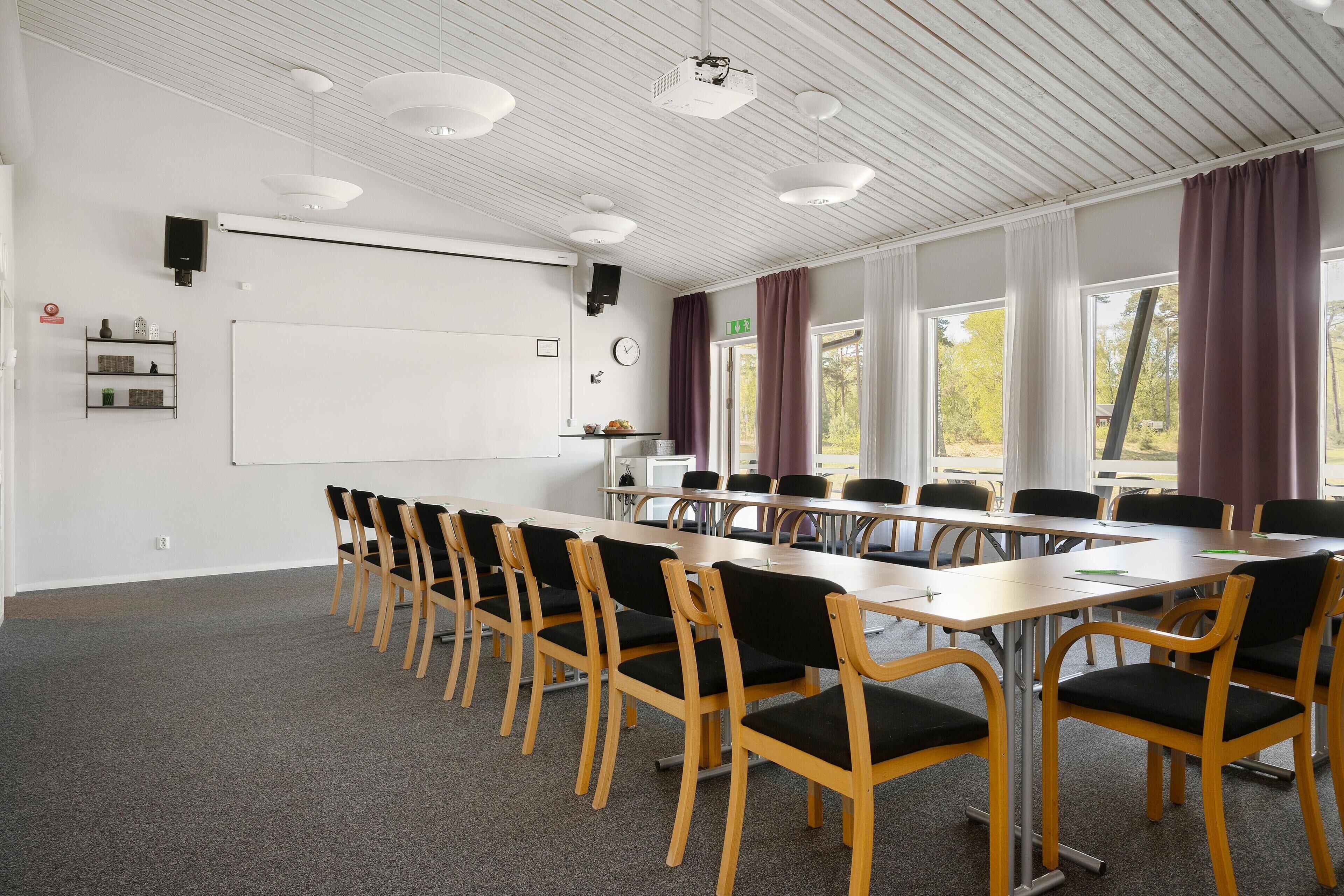 A conference room with a whiteboard, projector, and large windows with curtains.