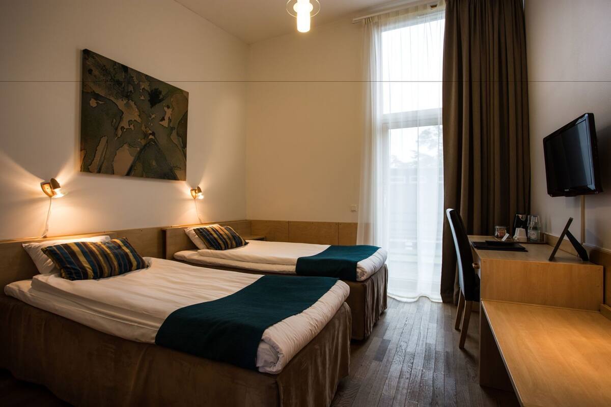 Een hotelkamer met twee bedden, een bureau, een televisie en een schilderij aan de muur.